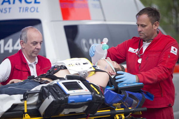 Notfallversorgung Patient auf Liege mit zwei Sanitätern vor Rettungsfahrzeug